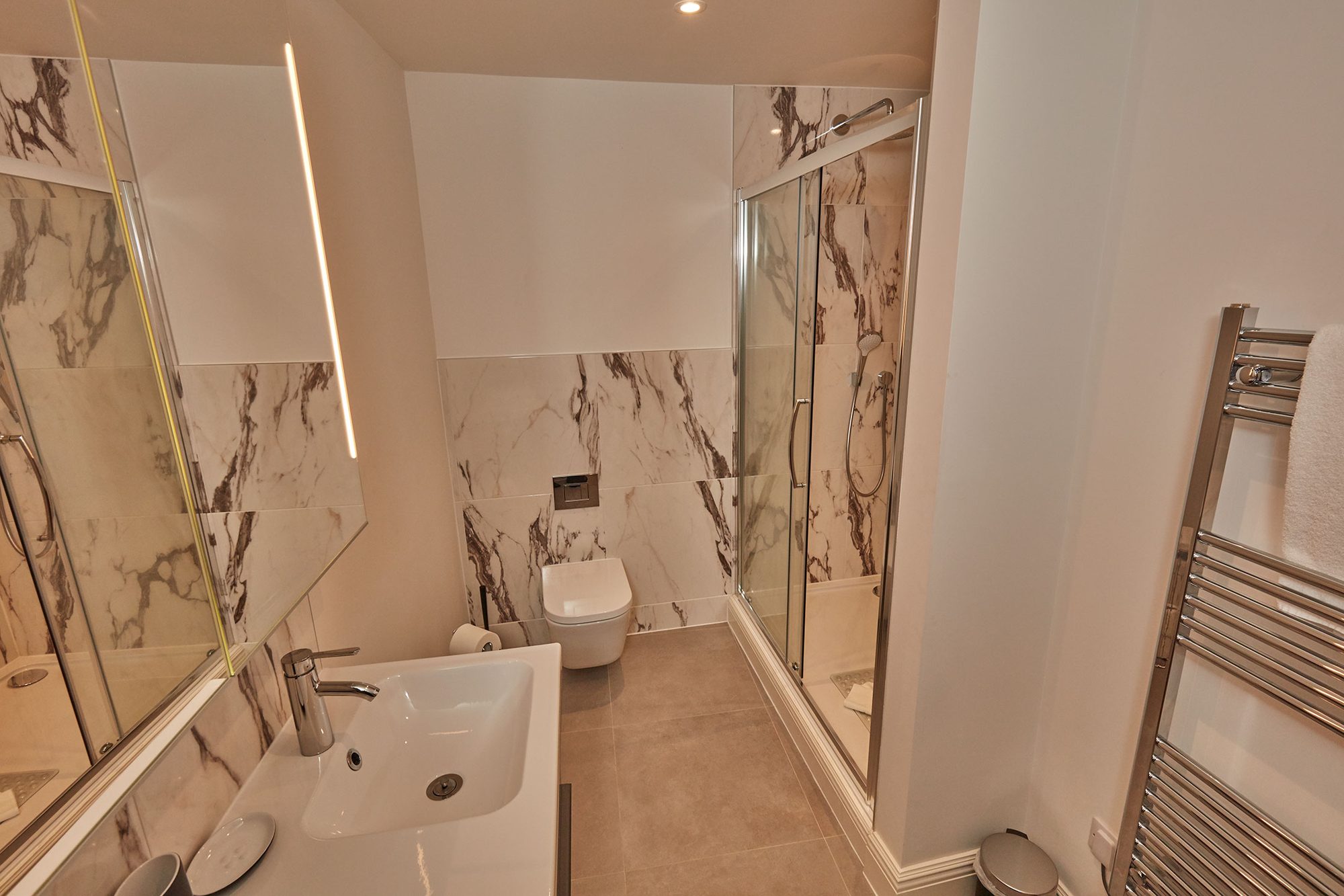 Marble-tiled shower room with walk-in shower and heated towel rail